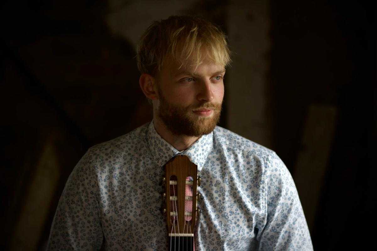 Andreas looking distant holding a guitar in front of him.